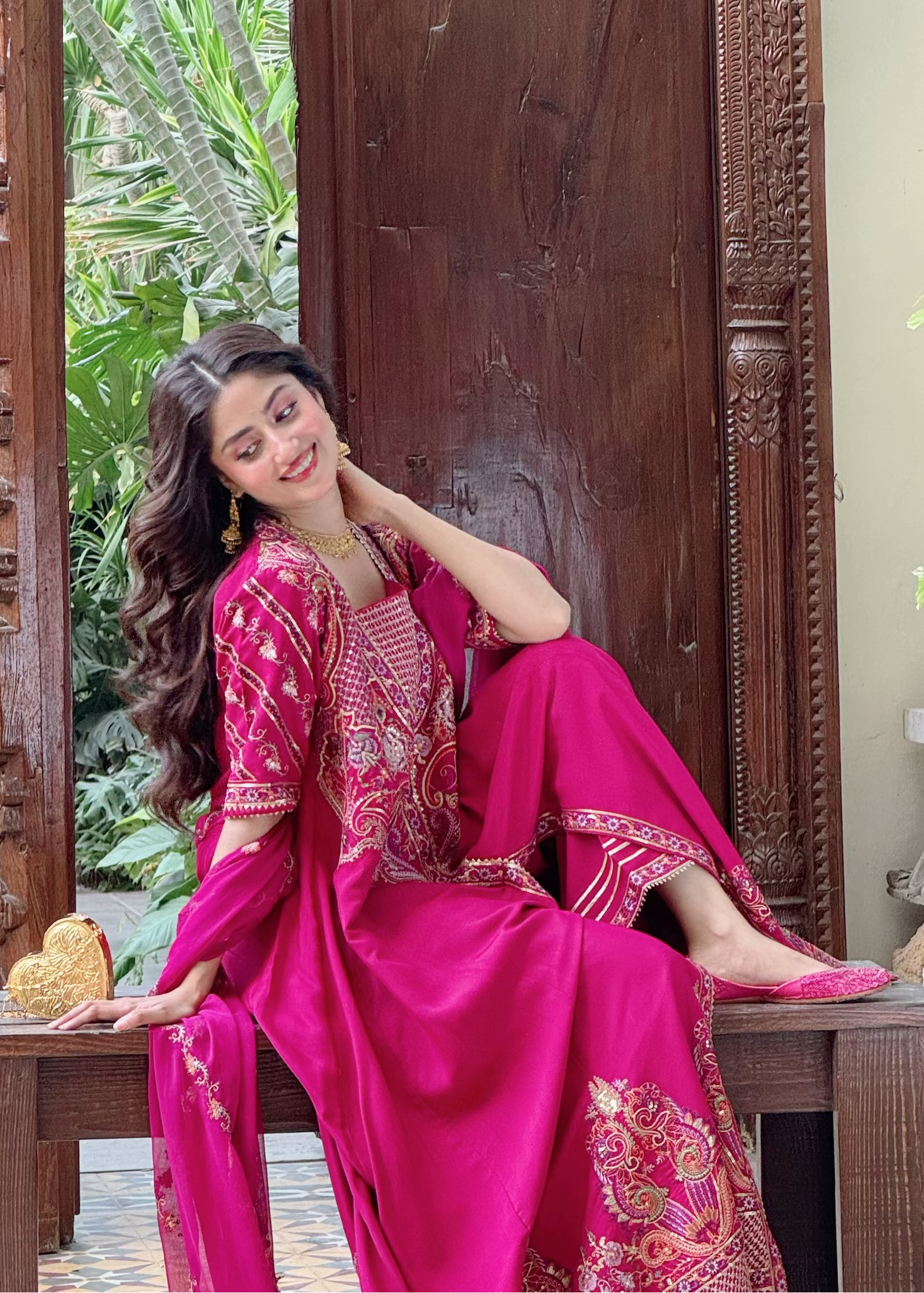 Sajal in a pink traditional outfit sitting on a wooden table with a decorative background