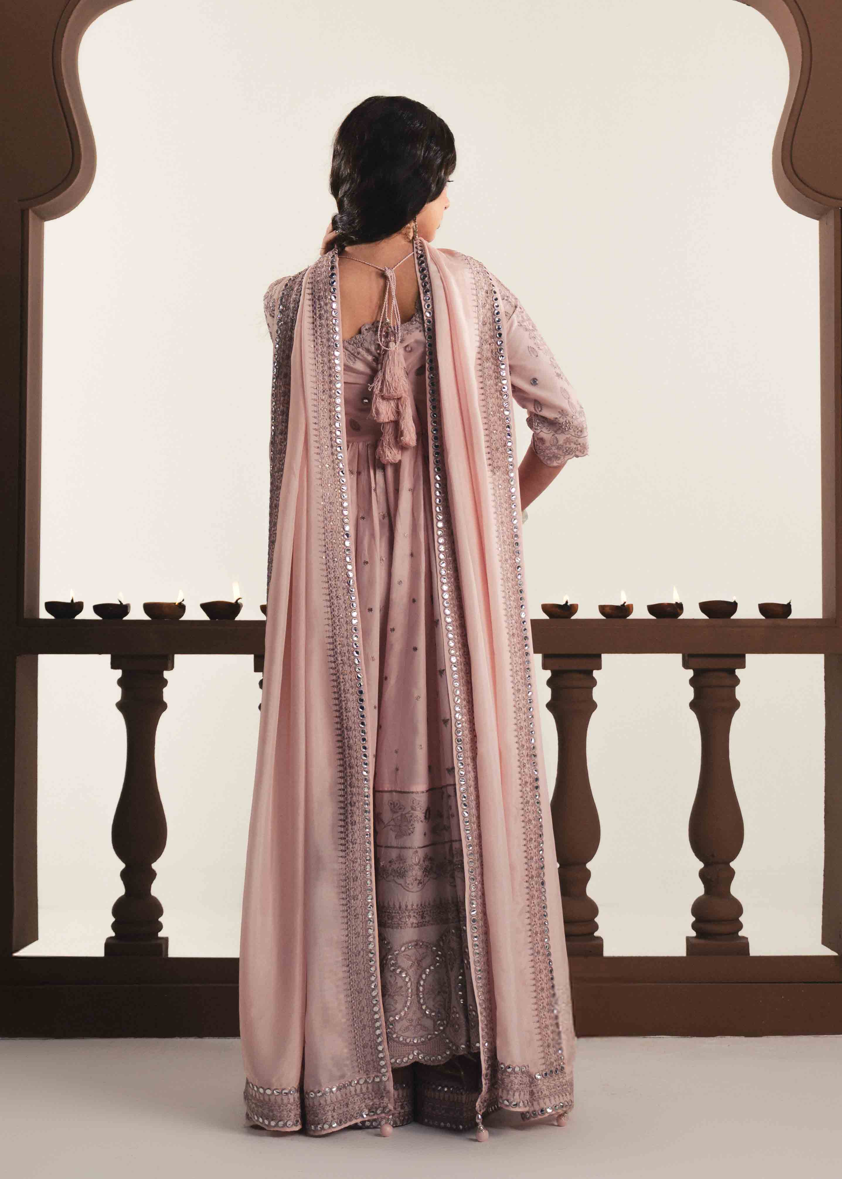 Woman wearing a long, light pink dress with a matching dupatta in front of a wooden archway.